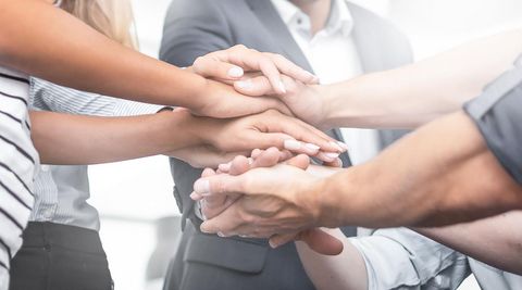 Das Bild zeigt ein Team, das einen Kreis bildet und die Hände als Zeichen der Gemeinschaft aufeinander legt.